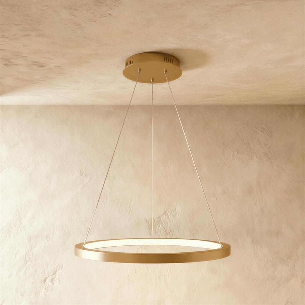 One golden ring pendant from Clérachic hangs on thin cables, framed by a soft sand-toned wall and ceiling.