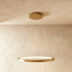 One golden ring pendant from Clérachic hangs on thin cables, framed by a soft sand-toned wall and ceiling.
