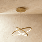 Clérachic's golden two-ring chandelier shows its rings overlapping in an X, lit warm above a textured room.