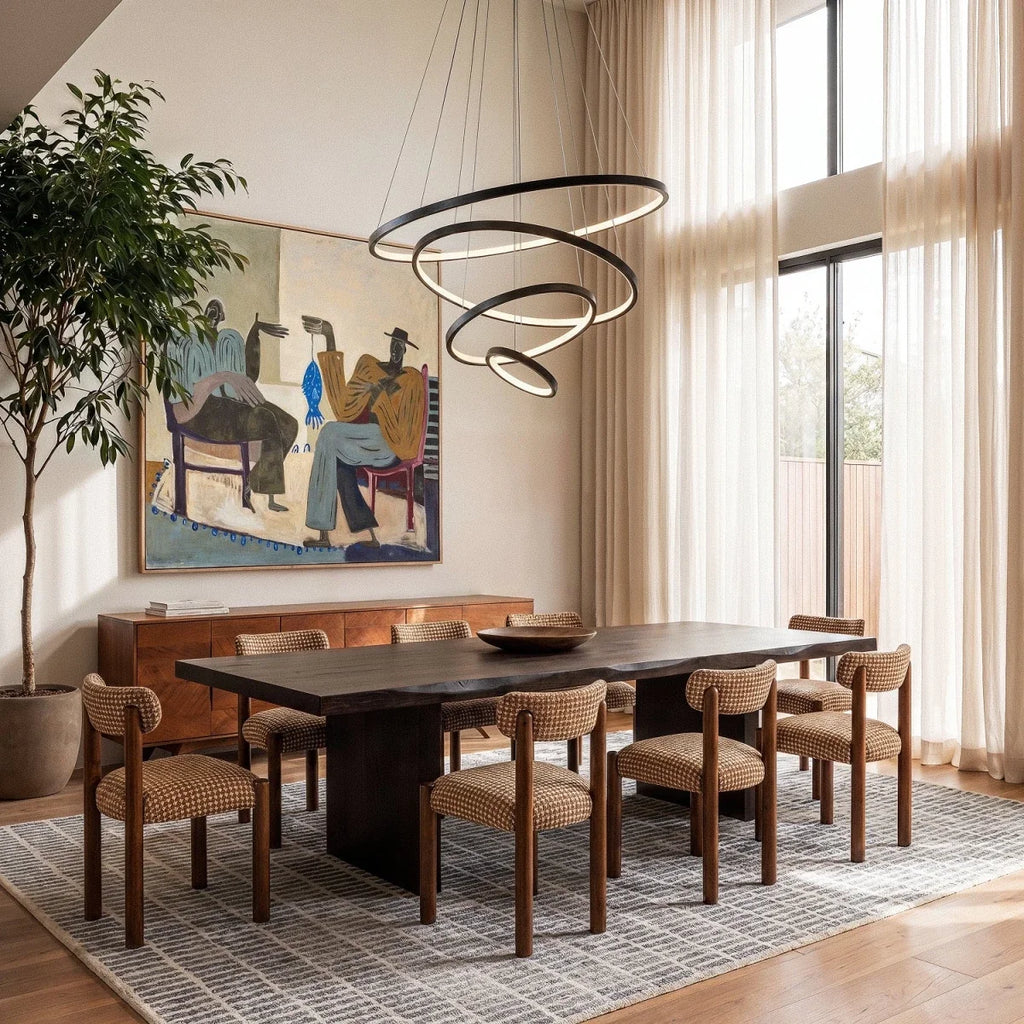 Clérachic's black four-ring chandelier hangs over a dark wood dining table set with woven chairs and framed art.