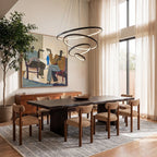 Clérachic's black four-ring chandelier hangs over a dark wood dining table set with woven chairs and framed art.