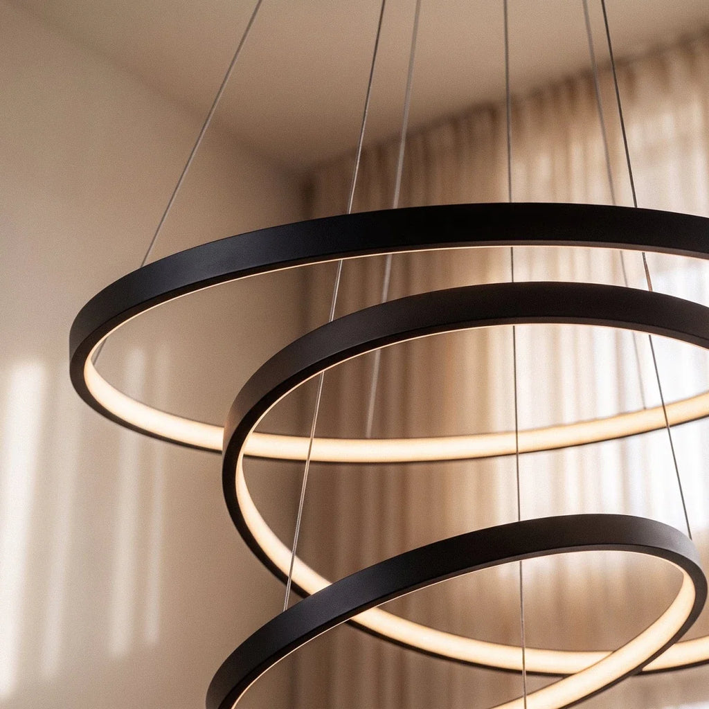 A close-up shows Clérachic's black rings cascading in a tight spiral, their LED edges glowing warm indoors.