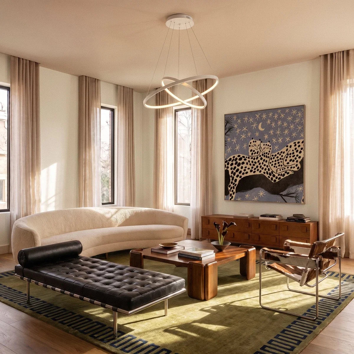 Clérachic's white two-ring pendant crosses above a curved sofa and patterned rug in a sunlit living room.