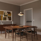 A Clérachic stacked ring pendant hangs over a walnut dining table with wishbone chairs, in a room with an abstract print.