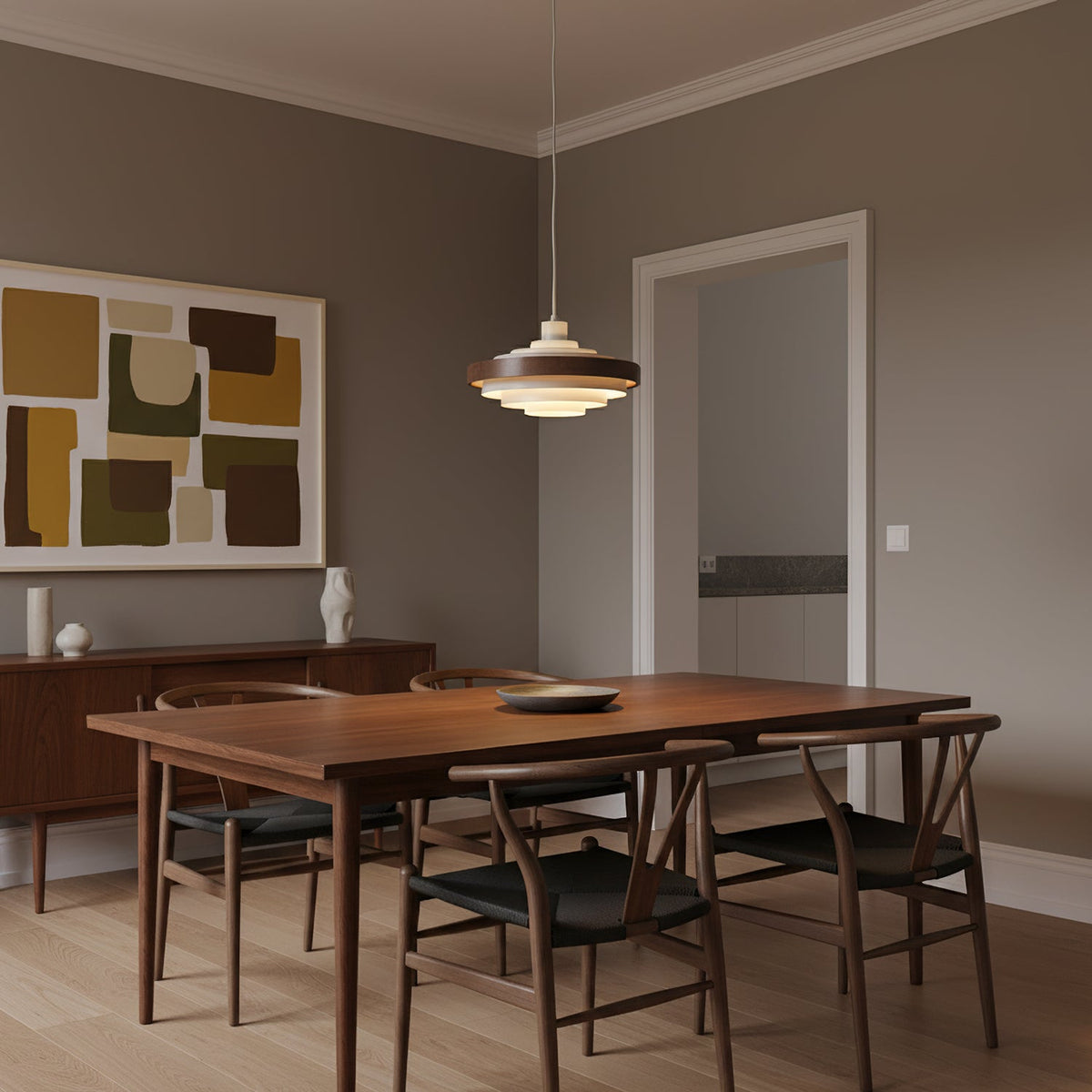 A Clérachic stacked ring pendant hangs over a walnut dining table with wishbone chairs, in a room with an abstract print.