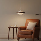 This Clérachic ring pendant lights a corner with a tan leather armchair and a round side table holding a cup and a book.