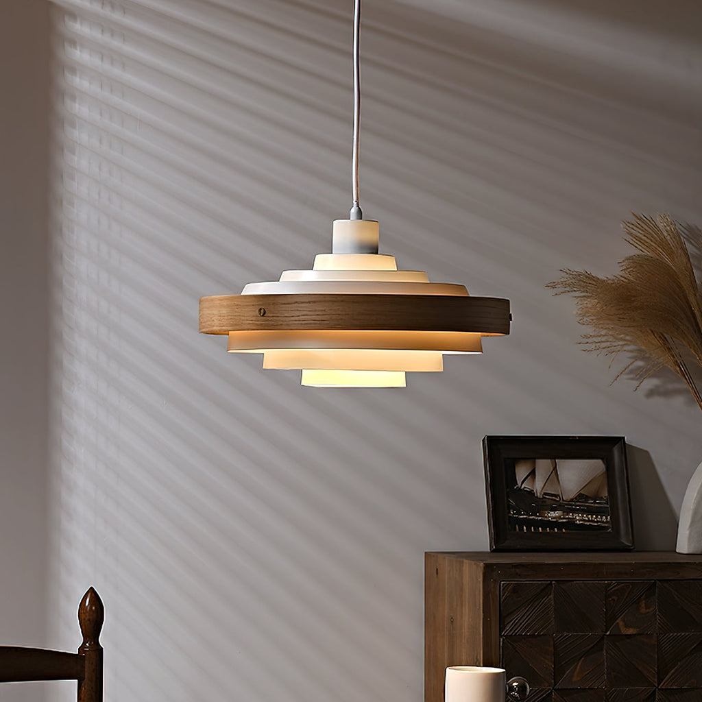 A white and walnut Clérachic stacked ring pendant glows warm in front of a striped shadow wall, with dried pampas grass beside it.