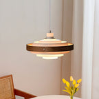 Close view of the lit tiers of a Clérachic ring pendant with a walnut band, above a table with yellow tulips and a cane chair.