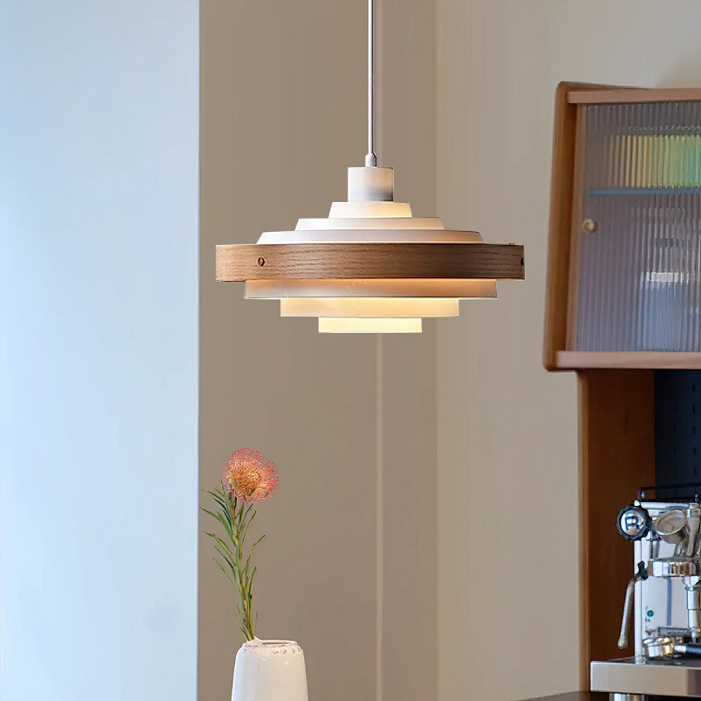 The lit tiers of a Clérachic white and walnut pendant in a room with a glass-fronted wood cabinet and a pink flower in a vase.