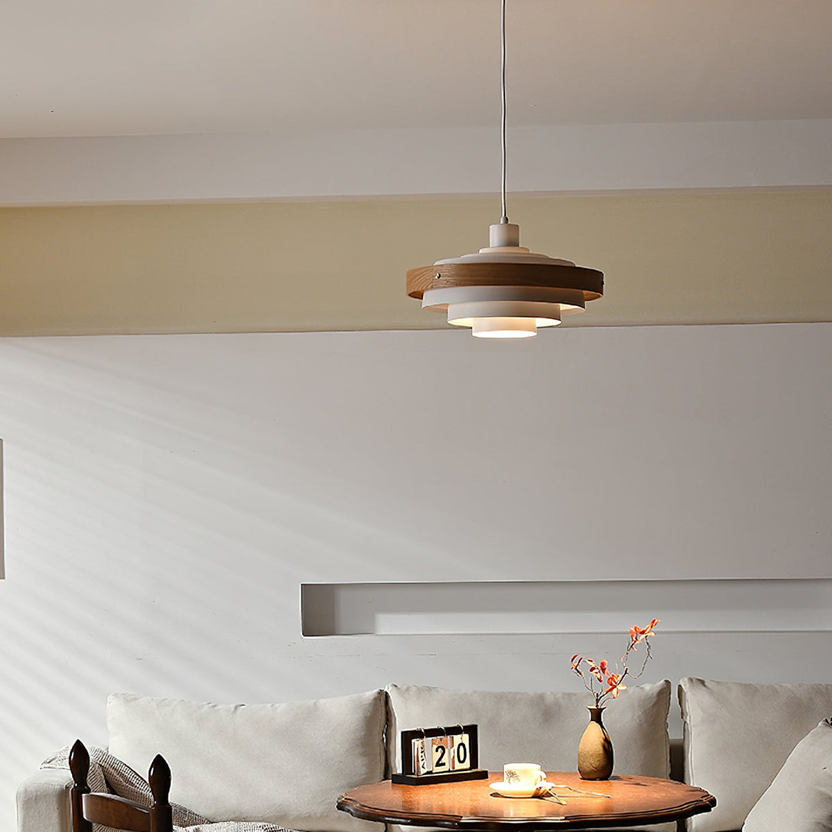 A Clérachic white and walnut pendant hangs high in a living room, above a low table and a pale sofa.