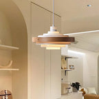 A Clérachic white and walnut pendant hangs under an arched ceiling, with an open kitchen and shelves in the background.