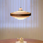 Close view of a Clérachic white and walnut pendant, lit, hung in front of pale vertical blinds above a small tea set.