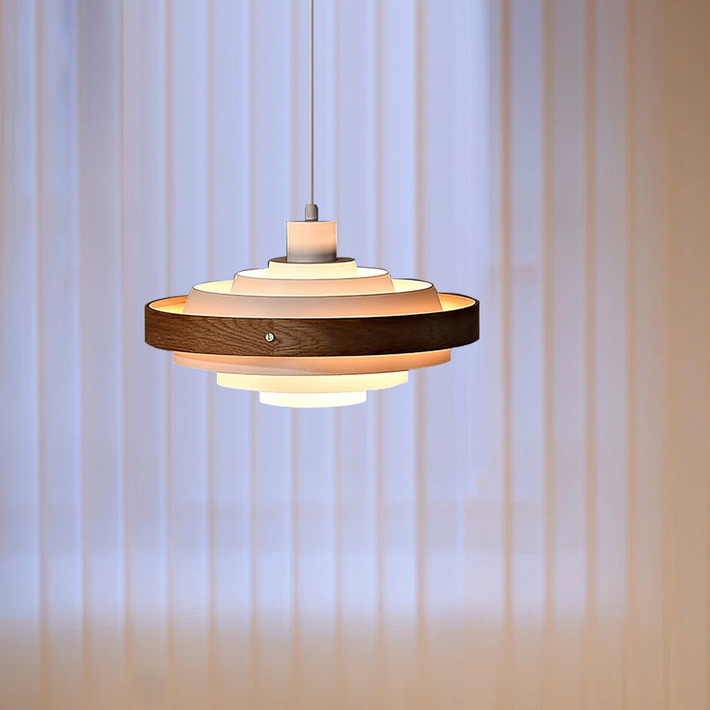 The tiers of this Clérachic walnut-banded pendant glow warm against softly lit vertical blinds.