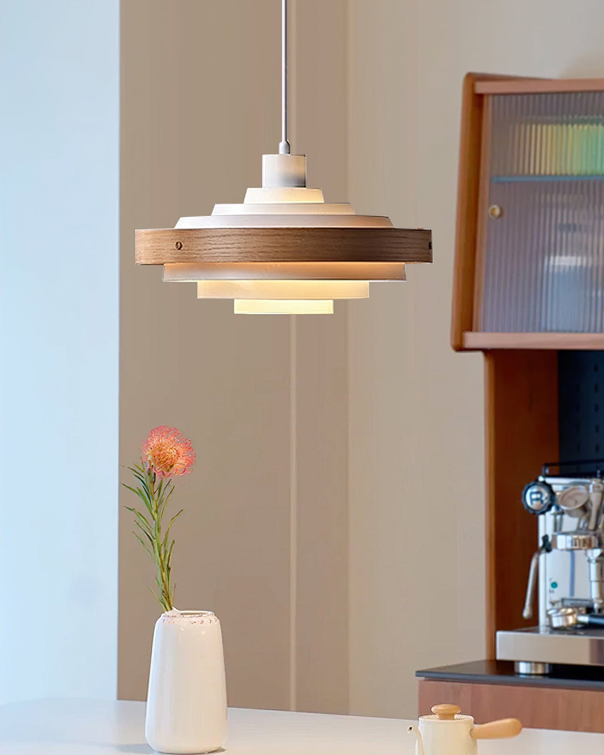 A Clérachic white and walnut pendant hangs by a window nook with a white vase, a pink flower and a coffee machine.