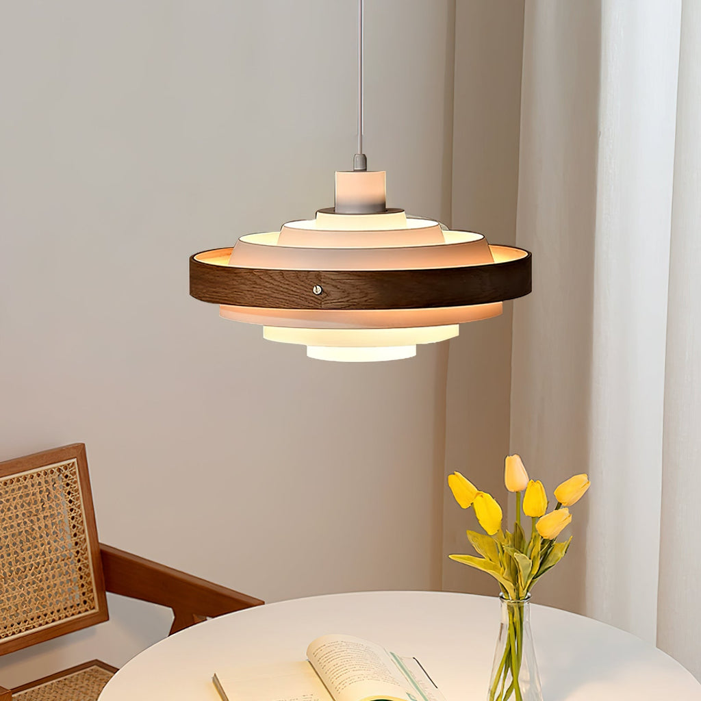 Close view of the lit tiers of this Clérachic pendant above a white round table with yellow tulips and an open book.