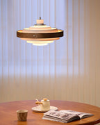 Clérachic white and walnut ring pendant, lit, above a wooden table with a teapot, a cup and a magazine.
