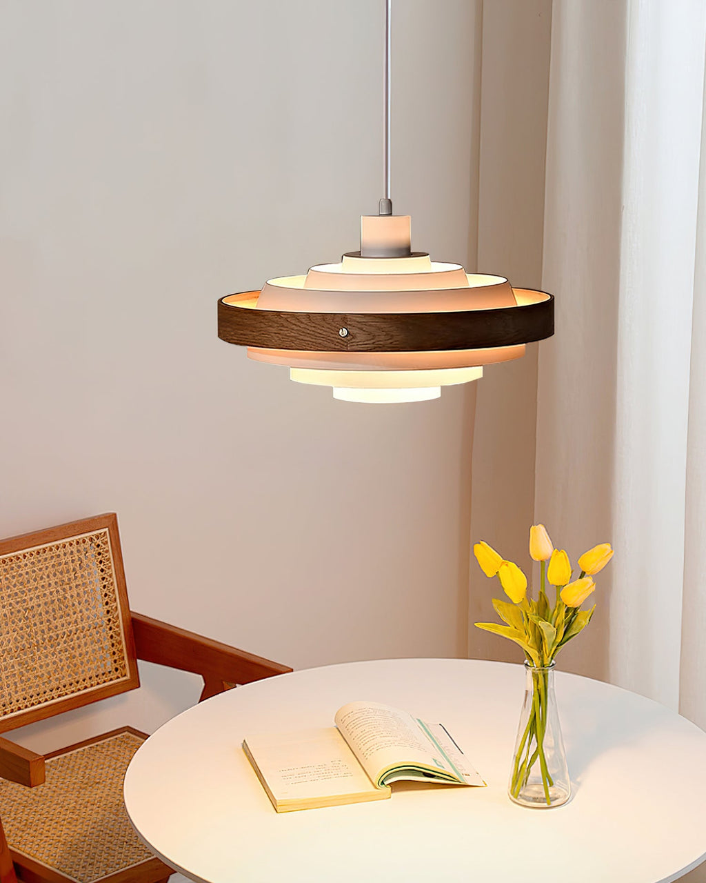 A Clérachic white and walnut pendant hangs above a round white table with an open book and a vase of yellow tulips.