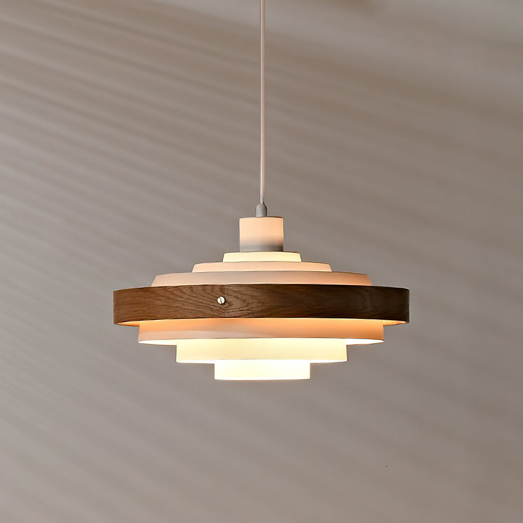 A lit Clérachic stacked ring pendant seen from slightly below, its warm light reaching the wall behind.