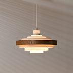 A lit Clérachic stacked ring pendant seen from slightly below, its warm light reaching the wall behind.