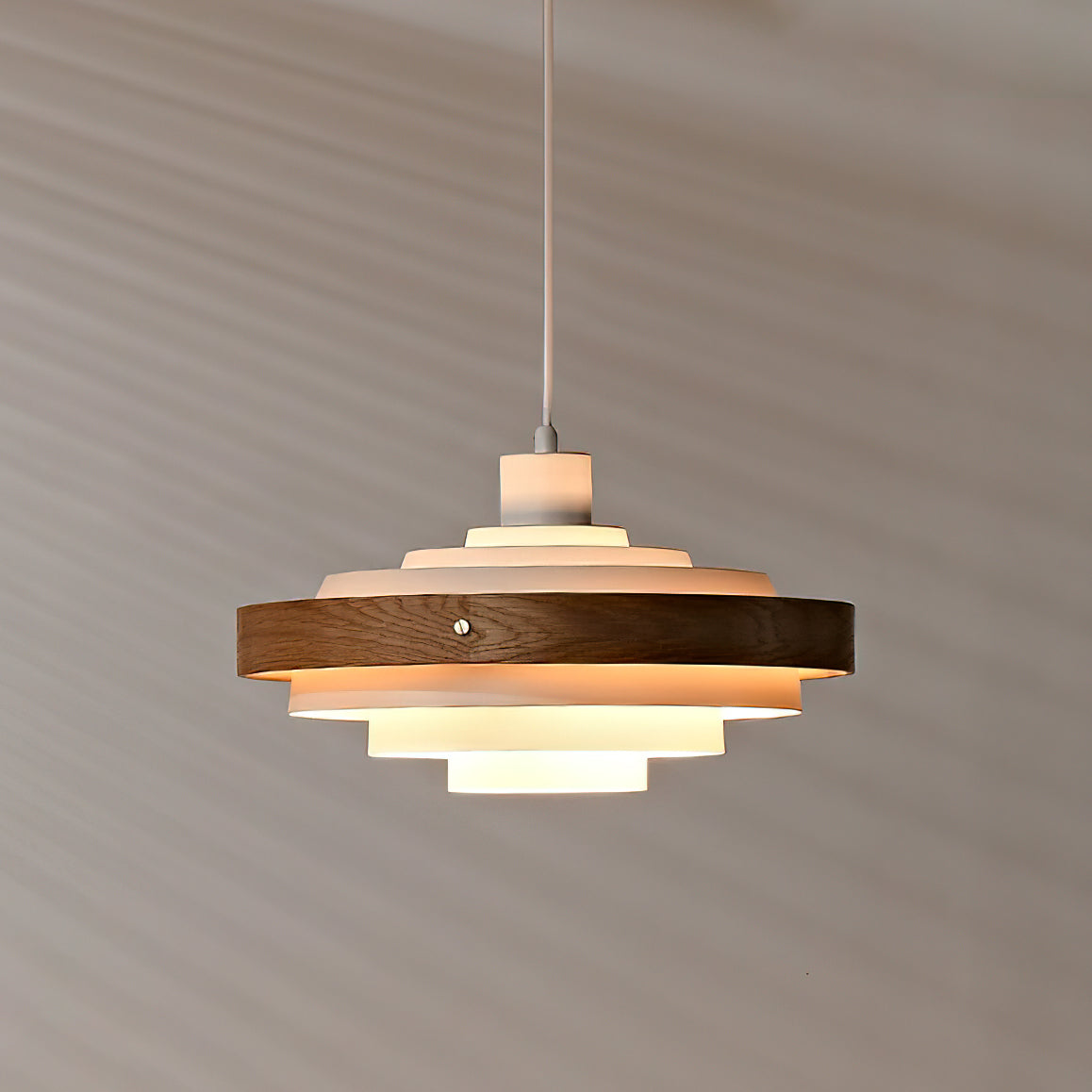 A lit Clérachic stacked ring pendant seen from slightly below, its warm light reaching the wall behind.