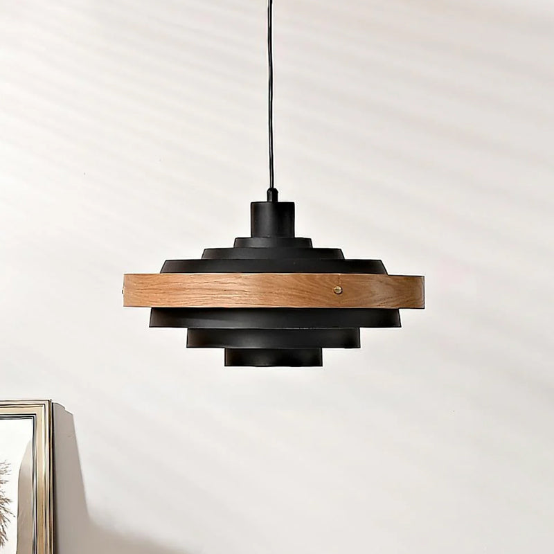 Black and oak Clérachic stacked ring pendant, hung from a black cord against a pale wall with a picture frame at the edge.