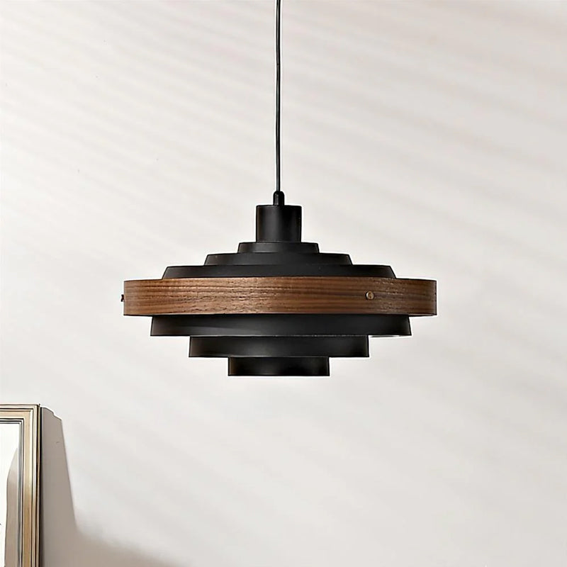 Black and walnut Clérachic pendant with a dark wood band on a black cord, against a pale wall.