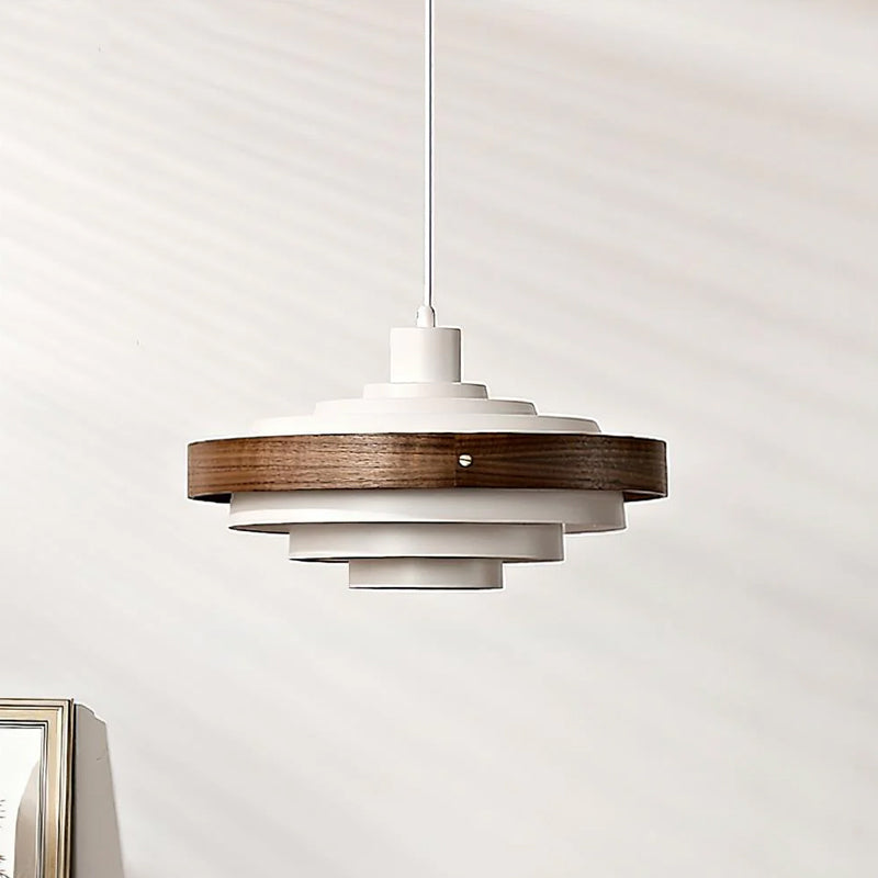White and walnut Clérachic stacked ring pendant on a white cord, its dark wood band around the top tiers, against a pale wall.