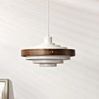 White and walnut Clérachic stacked ring pendant on a white cord, its dark wood band around the top tiers, against a pale wall.