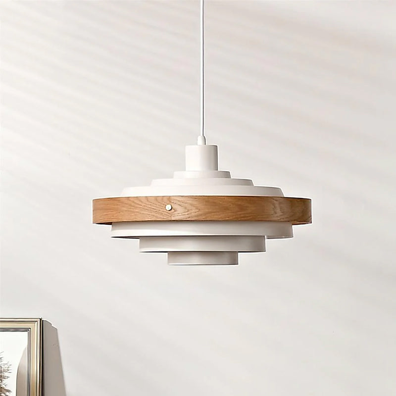 A Clérachic white and oak stacked ring pendant on a white cord, the pale oak band around the upper tiers, against a light wall.