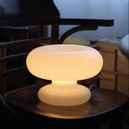 The Clérachic donut lamp glowing amber on a dark wooden seat, with the stacked frosted shade and base lit from within.