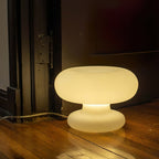 A lit Clérachic donut table lamp on an old wooden floor beside a dark door frame, casting a warm pool of light.