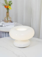 A Clérachic donut lamp glowing softly on a marble-topped table, with a small vase of orange and yellow flowers behind it.