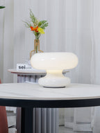 Clérachic donut lamp glowing on a marble table, with sheer curtains and a flower vase in a gold stand behind it.