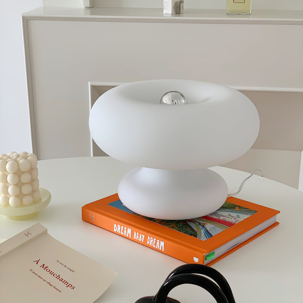 White Clérachic donut lamp on an orange book on a white table, with a silver-tipped bulb visible in the centre of the ring.