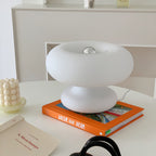 White Clérachic donut lamp on an orange book on a white table, with a silver-tipped bulb visible in the centre of the ring.