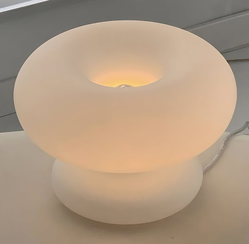 Close view of the frosted glass donut shade of this Clérachic lamp, glowing warmly around the bulb at the centre of the ring.