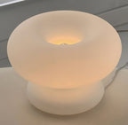 Close view of the frosted glass donut shade of this Clérachic lamp, glowing warmly around the bulb at the centre of the ring.