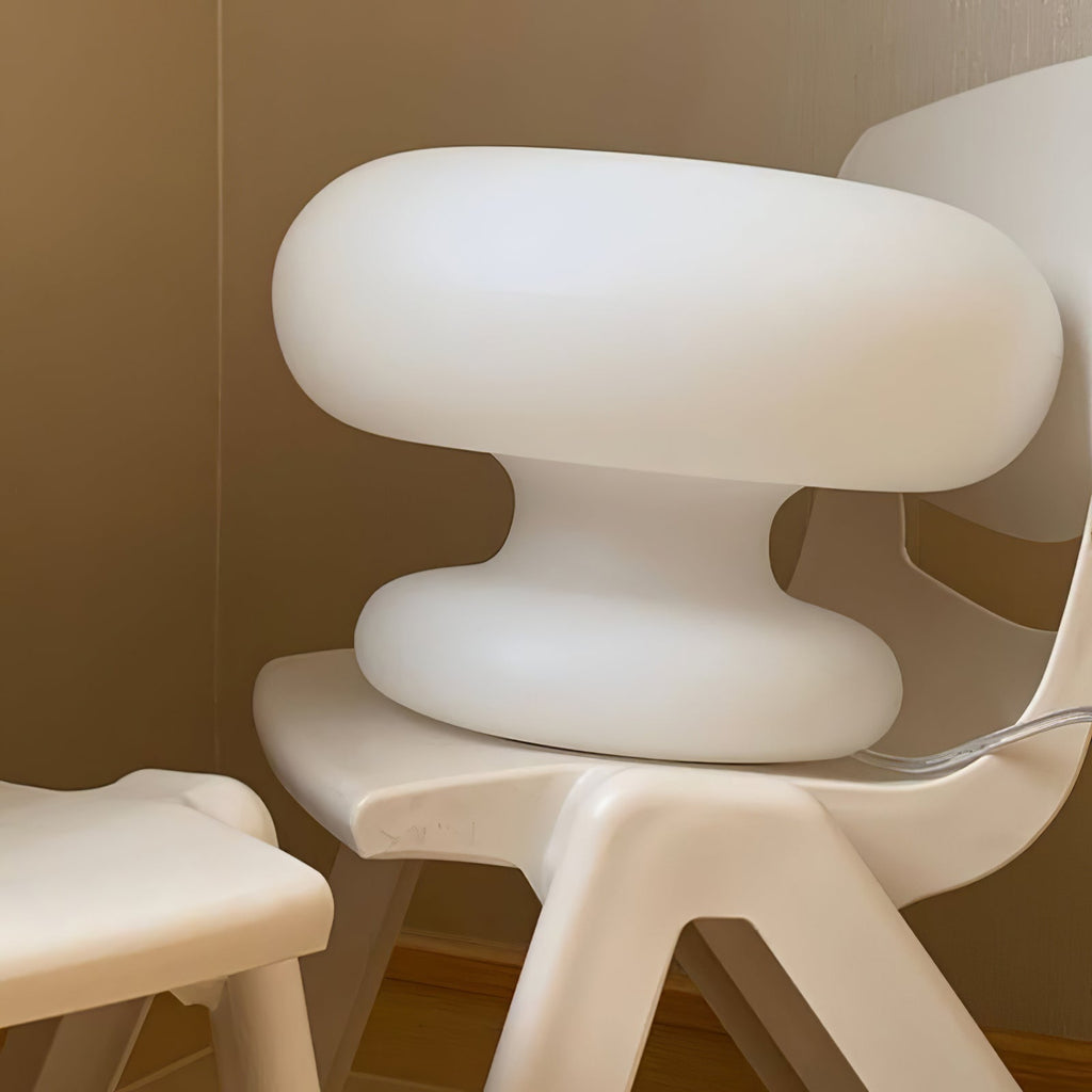 Close view of the matt white glass of the Clérachic donut lamp, set on a white moulded chair against a beige wall.