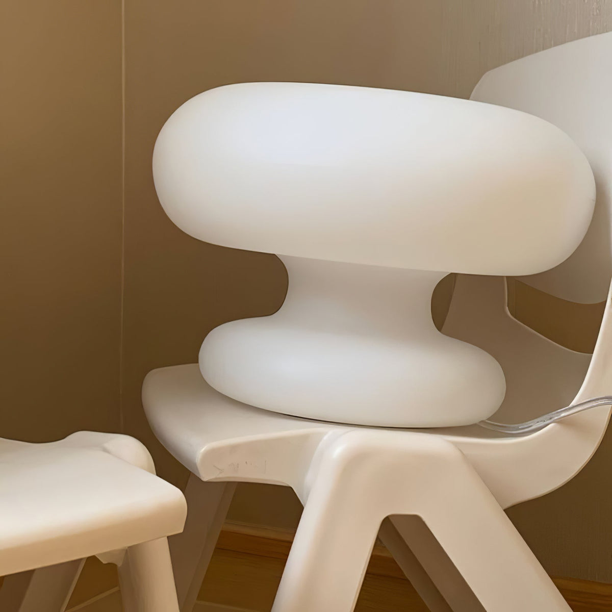 Close view of the matt white glass of the Clérachic donut lamp, set on a white moulded chair against a beige wall.