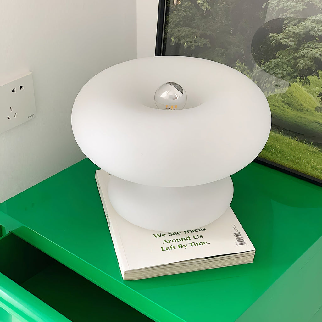 White Clérachic donut lamp on a paperback on a bright green shelf, with a silver-tipped bulb showing in the centre.