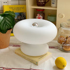 Clérachic donut lamp on a yellow book on a kitchen counter, with a large-leaf plant, a glass jar of biscuits and a lemon.