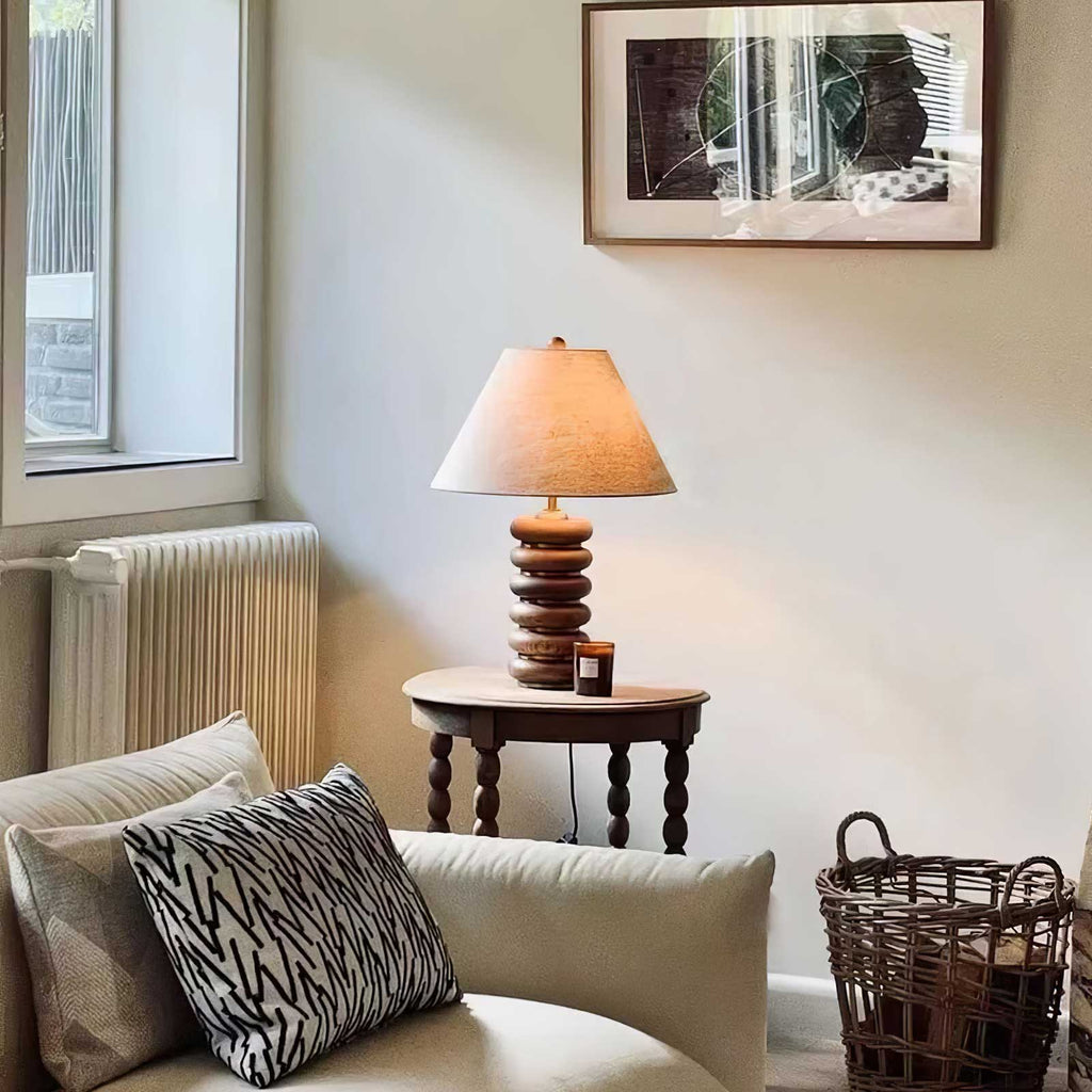 A Clérachic table lamp glows on a small turned-leg side table beside a cream sofa, a radiator and a striped cushion.