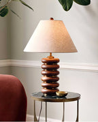 Close view of this Clérachic table lamp on a round side table, with a brass dish and a rust-red chair at its edge.