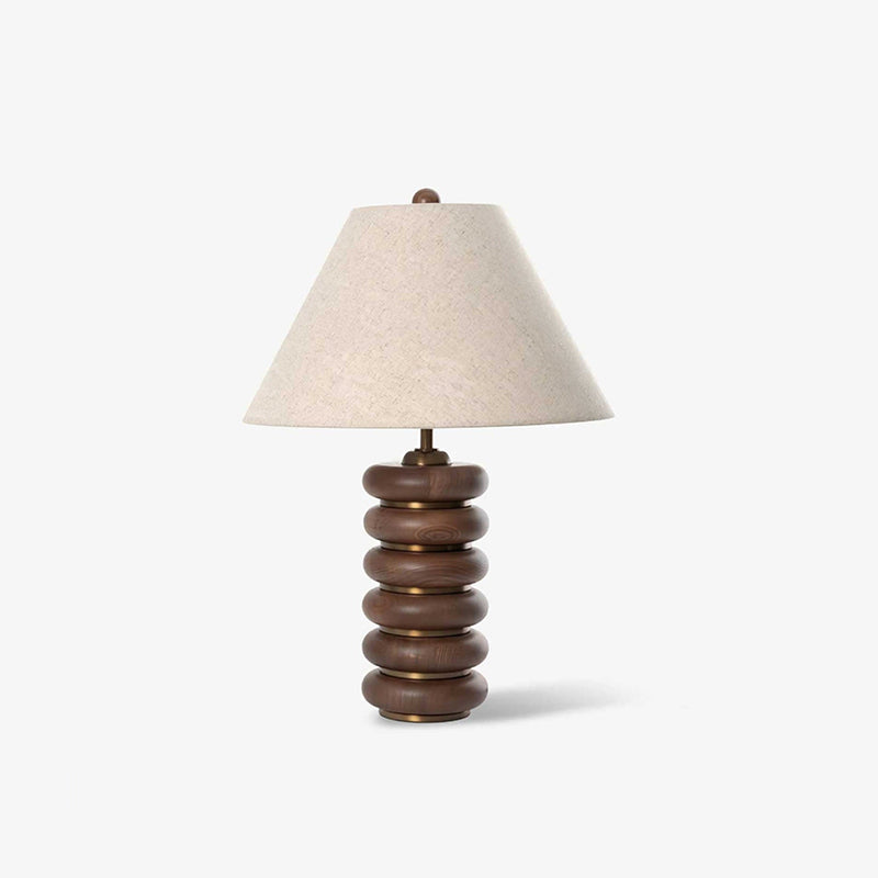 This Clérachic table lamp on a pale grey backdrop, its stacked walnut base banded in gold under a white linen shade.