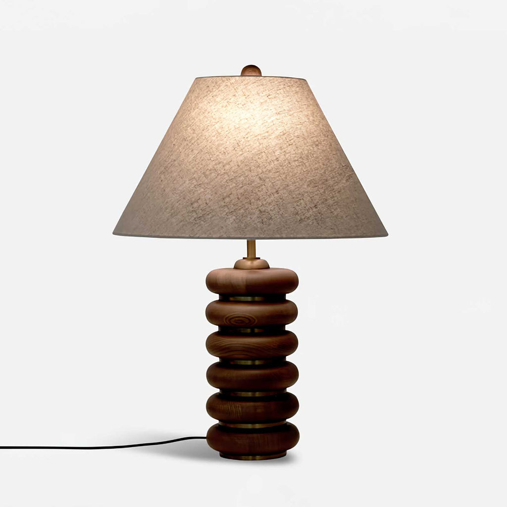 This Clérachic table lamp lit on a white backdrop, with its black cord trailing from the walnut base across the floor.