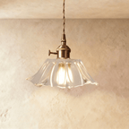 Clérachic clear ribbed glass pendant with a flared hem, brass switch holder and twisted cord, glowing warmly against a limewashed wall.