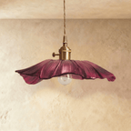 Clérachic wide purple glass pendant with a rippled petal edge, brass switch holder and a clear bulb below, on a limewashed wall.