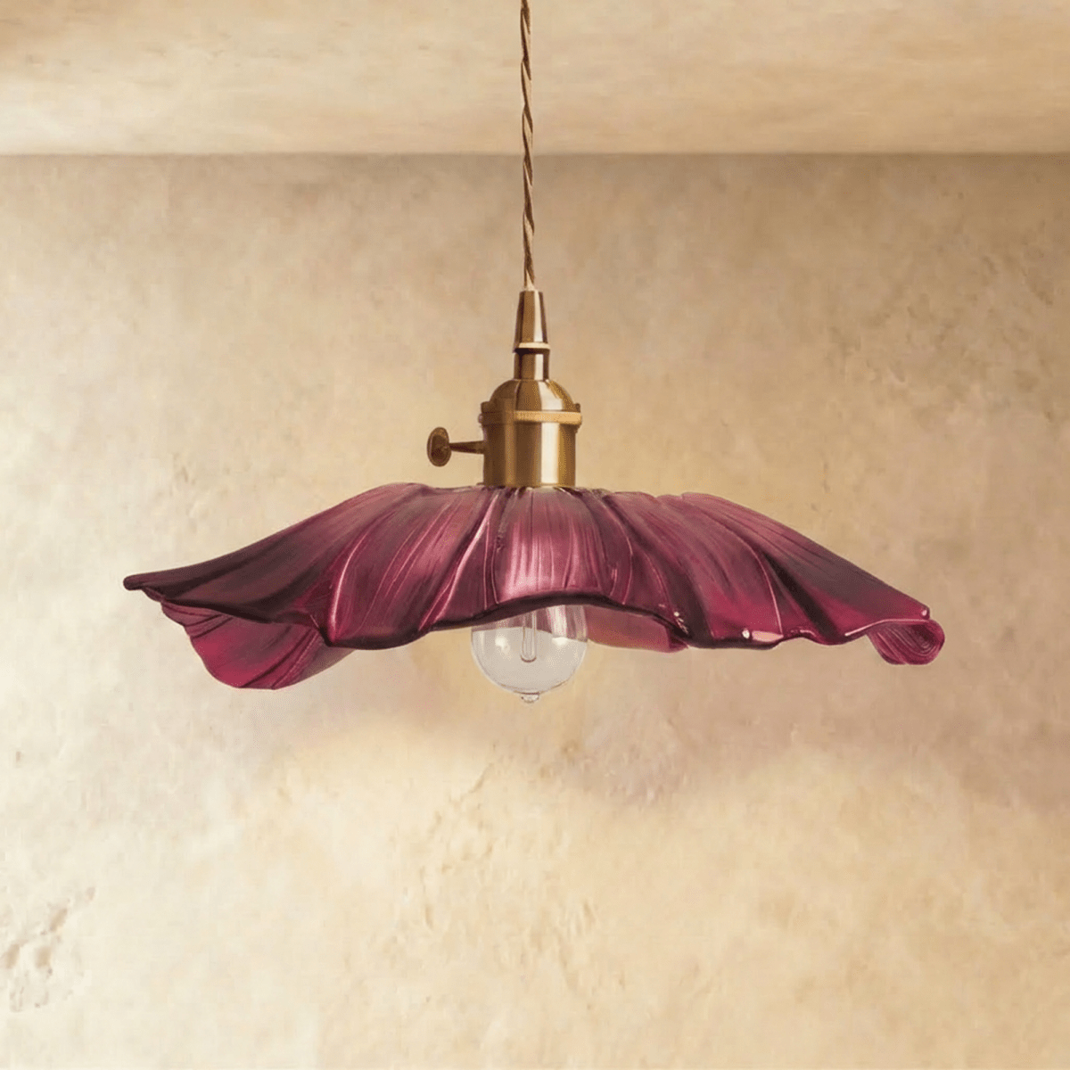 Clérachic wide purple glass pendant with a rippled petal edge, brass switch holder and a clear bulb below, on a limewashed wall.