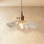Clérachic wide clear glass pendant with a gently waved rim, brass switch holder and a glowing bulb, against a soft limewashed wall.