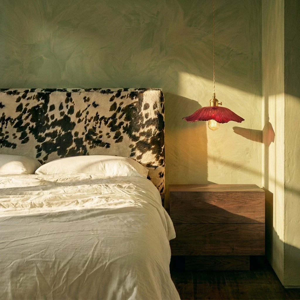 Clérachic red glass pendant with a flared shade hung beside a walnut bedside unit, in a bedroom with sage plaster walls and low sun.
